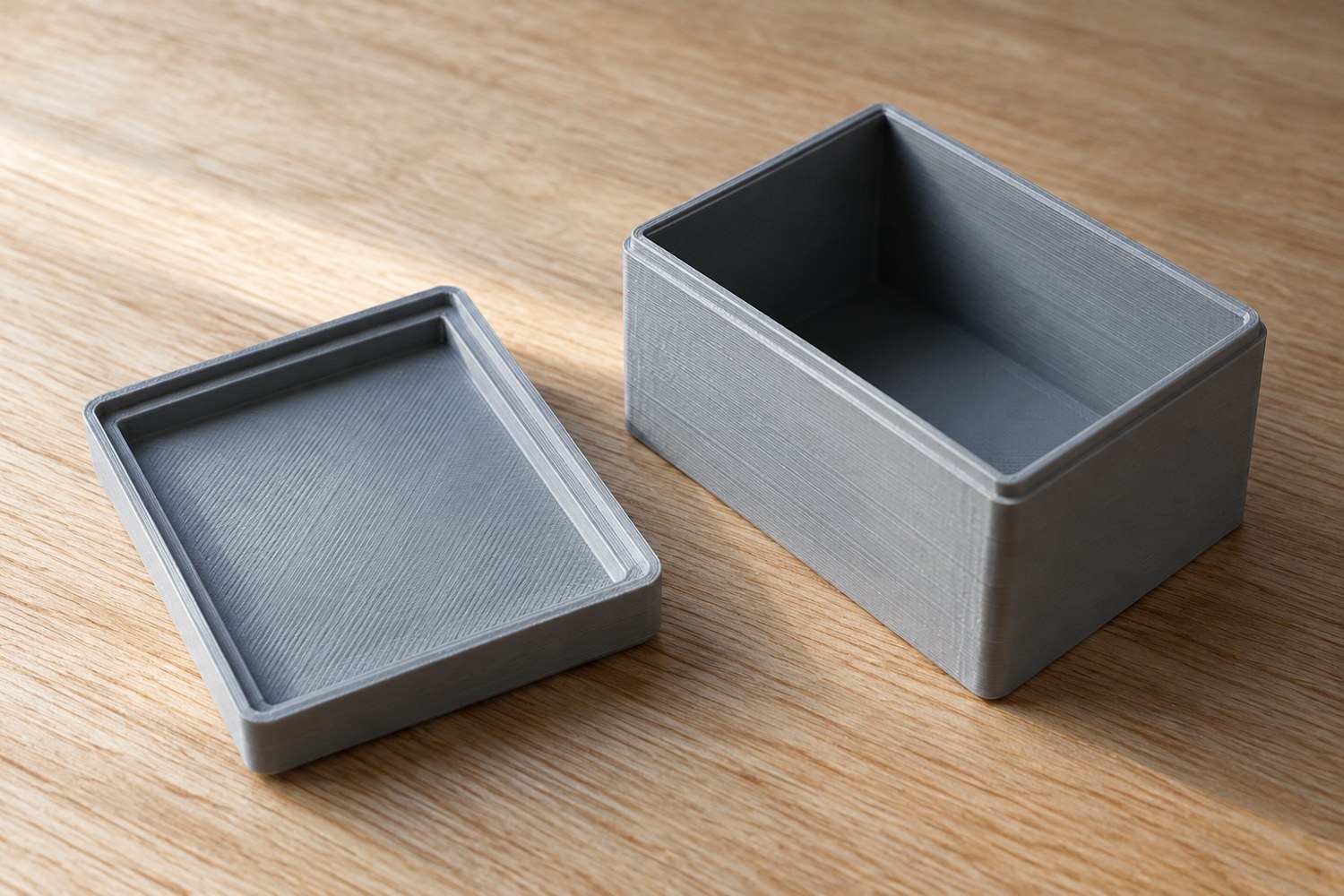 Illustration: A small grey 3D-printed storage box and its removable lid shown apart, close view of the shallow locating lip inside the lid and corresponding box rim, plain tabletop